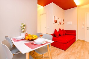 Een eetruimte met een tafel gedekt voor twee personen, een rode bank en een wand met ingelijste kunstwerken.