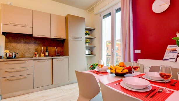 Una cucina moderna con mobili beige, forno integrato e zona pranzo con tovaglia rossa.