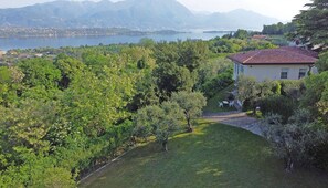 Une maison avec un toit recouvert de tuiles rouges, entourée d’une végétation luxuriante et avec un lac en arrière-plan.