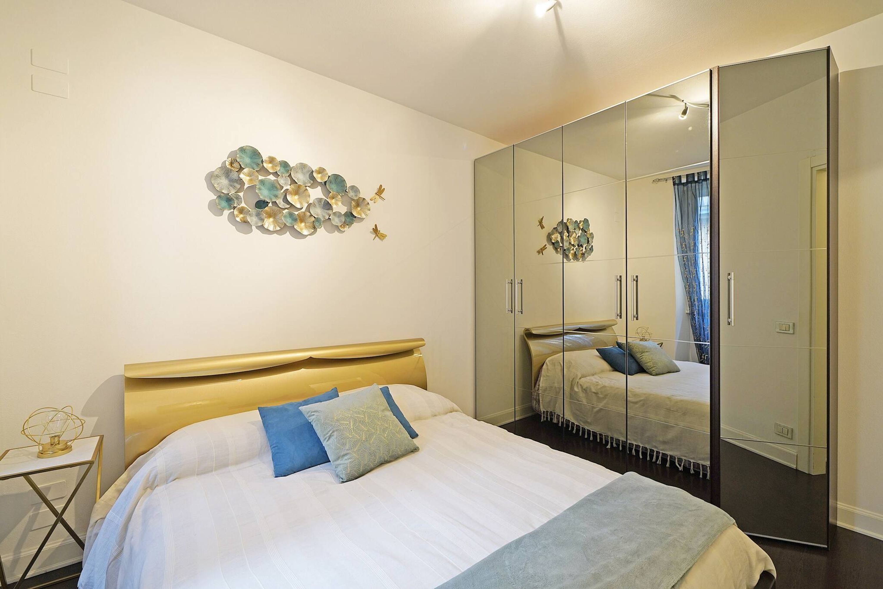 A modern bedroom with a large bed, a bedside table, a wall art piece, and a large mirror.
