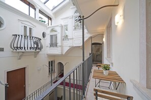 Een meerlaags interieur met een houten bankje, een potplant, witte muren en een trap.