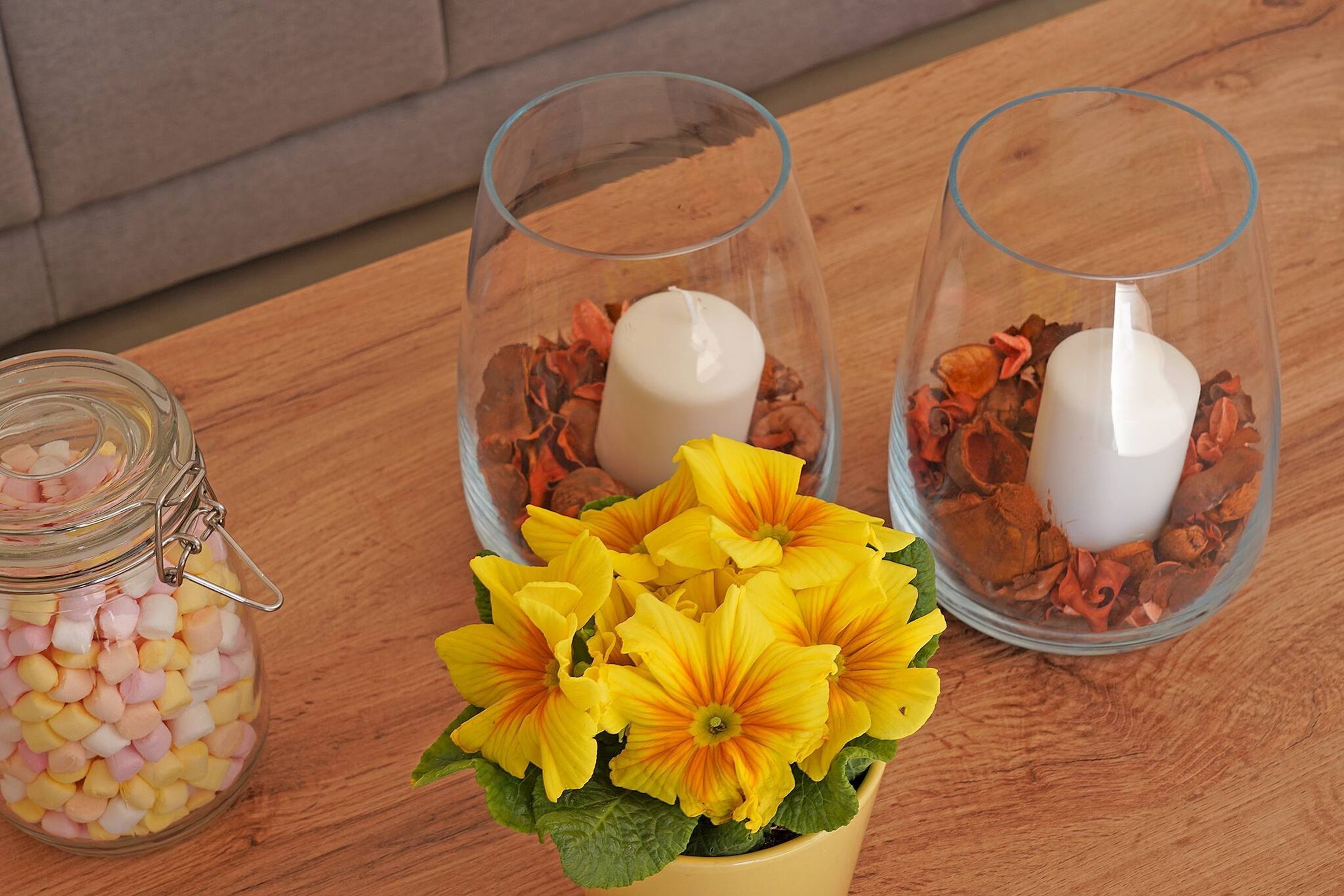 Two glass candle holders with candles and dried flowers on a wooden table.
