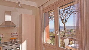 Une cuisine équipée d’une cuisinière à gaz, d’un luminaire suspendu et offrant une vue sur un balcon avec une chaise.