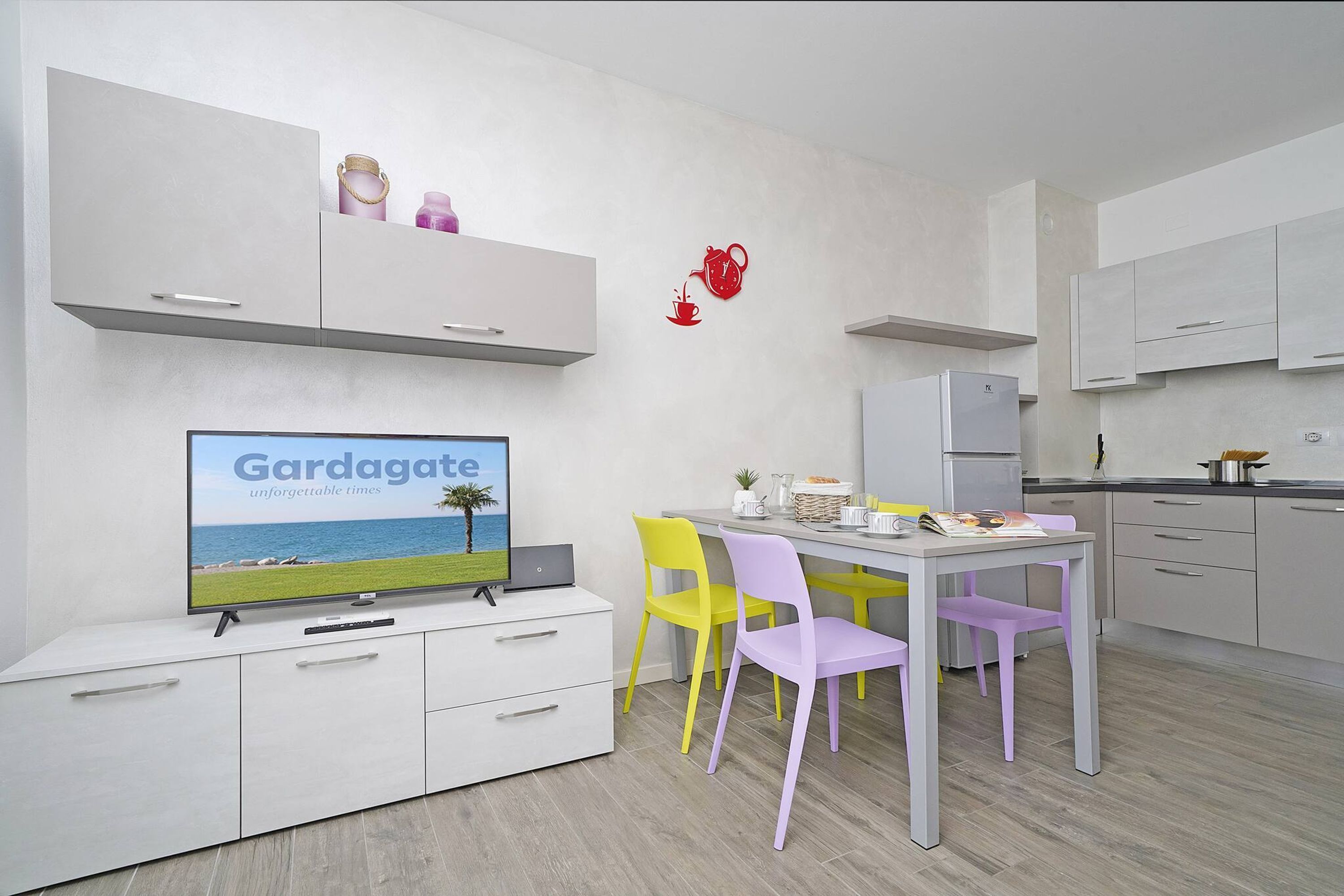A modern kitchen with white cabinets, a dining table with chairs, and a television displaying 'Gargagate'.