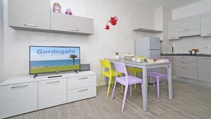 Una cocina moderna con armarios blancos, una mesa de comedor con sillas y un televisor que muestra 'Gargagate'.