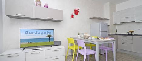 A modern kitchen with white cabinets, a dining table with chairs, and a television displaying 'Gargagate'.