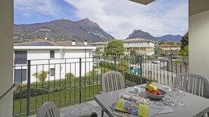 Un balcón con mesa lista para comer, un bol de fruta y vistas a casas y montañas.