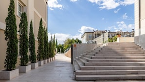 Un edificio con una escalera que sube a un piso superior, rodeado de árboles en macetas y un cielo despejado.
