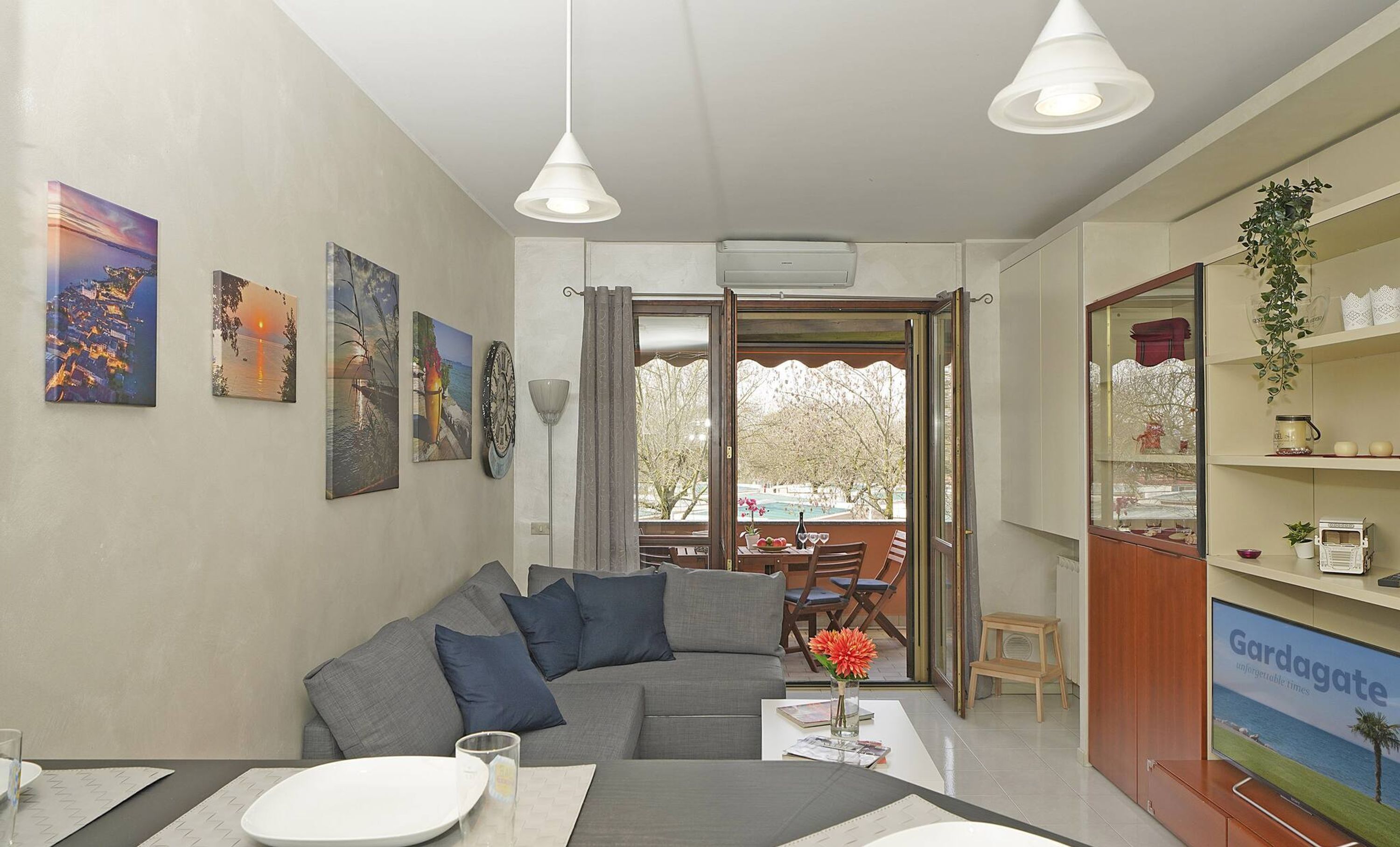 Una sala de estar con un sofá gris, una mesa de comedor con un florero y un televisor sobre un mueble de madera.