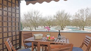 A wooden table with chairs, a basket labeled "Home," a bowl of fruit, a potted plant, and wine glasses on a balcony overlooking a snowy landscape with trees. - Casa Rudi in Sirmione (Sirmione)