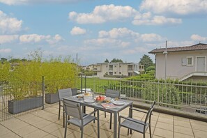 Un balcón con una mesa lista para comer, rodeado de sillas y vista a una zona residencial con casas y vegetación.