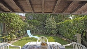 Un patio cubierto con una mesa para dos, rodeado de abundante vegetación y una silla blanca.
