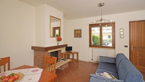 Una sala de estar con chimenea, un sofá, una mesa de comedor con fruta y un ventanal con vistas al exterior.