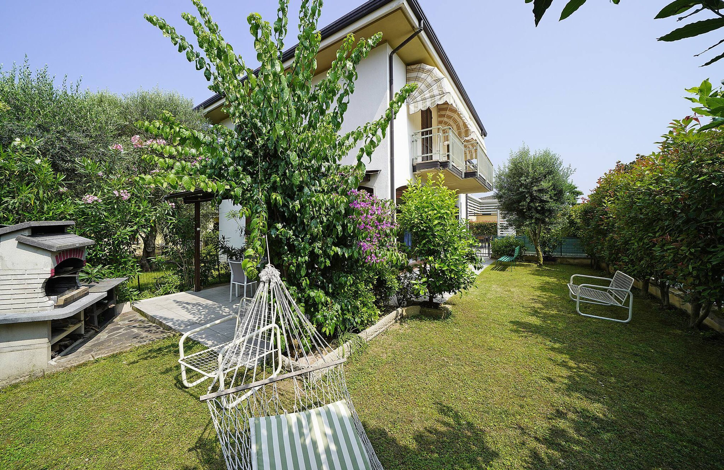 Un jardin avec un hamac, un espace barbecue et un bâtiment doté d’un balcon.