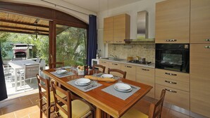 A modern kitchen with wooden cabinets, a built-in oven, and a dining area with a table set for two. - Casa Della Bougan-ville (Toscolano Maderno)