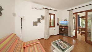 A room with a sofa, a glass coffee table, a radiator, a window with curtains, and a view of the sea. - Casa Della Bougan-ville (Toscolano Maderno)