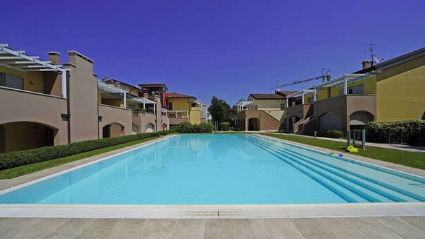 Una piscina circondata da palazzi con balconi e un cielo azzurro terso.
