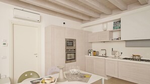 Una cucina moderna con mobili bianchi, forno a incasso, microonde e piano cottura a gas. Si nota un tavolo da pranzo con sedie e un cesto di pane.