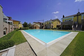 Ein Swimmingpool, umgeben von einer gepflegten Rasenfläche und einer Reihe bunter Häuser.