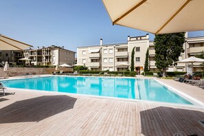A swimming pool with sun loungers and umbrellas, surrounded by apartment buildings. - Fasanella 50 in Toscolano-maderno (Toscolano Maderno)