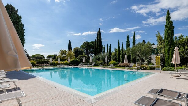 A swimming pool with lounge chairs and umbrellas, surrounded by trees and greenery. - Fasanella 50 in Toscolano-maderno (Toscolano Maderno)