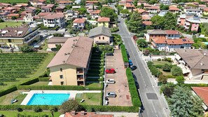 An aerial view of a residential area with a large building featuring a swimming pool, a parking lot, and a street with parked cars. - Susie s Place in Sirmione (Sirmione)