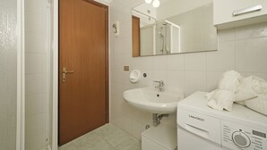 Un baño con puerta de madera, un lavabo blanco, un espejo y una lavadora.