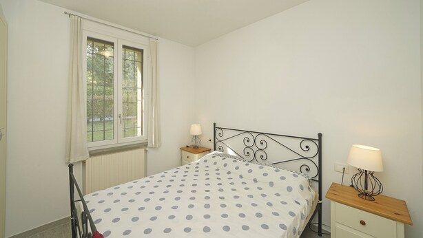 Ein Schlafzimmer mit einem Bett, zwei Nachttischen, einem Fenster und einer Heizung.