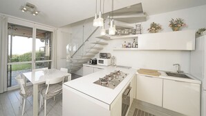 Eine moderne Küche mit einer zentralen Kochinsel, einem Essbereich mit einem Glastisch und einer Treppe, die zu einer oberen Ebene führt.
