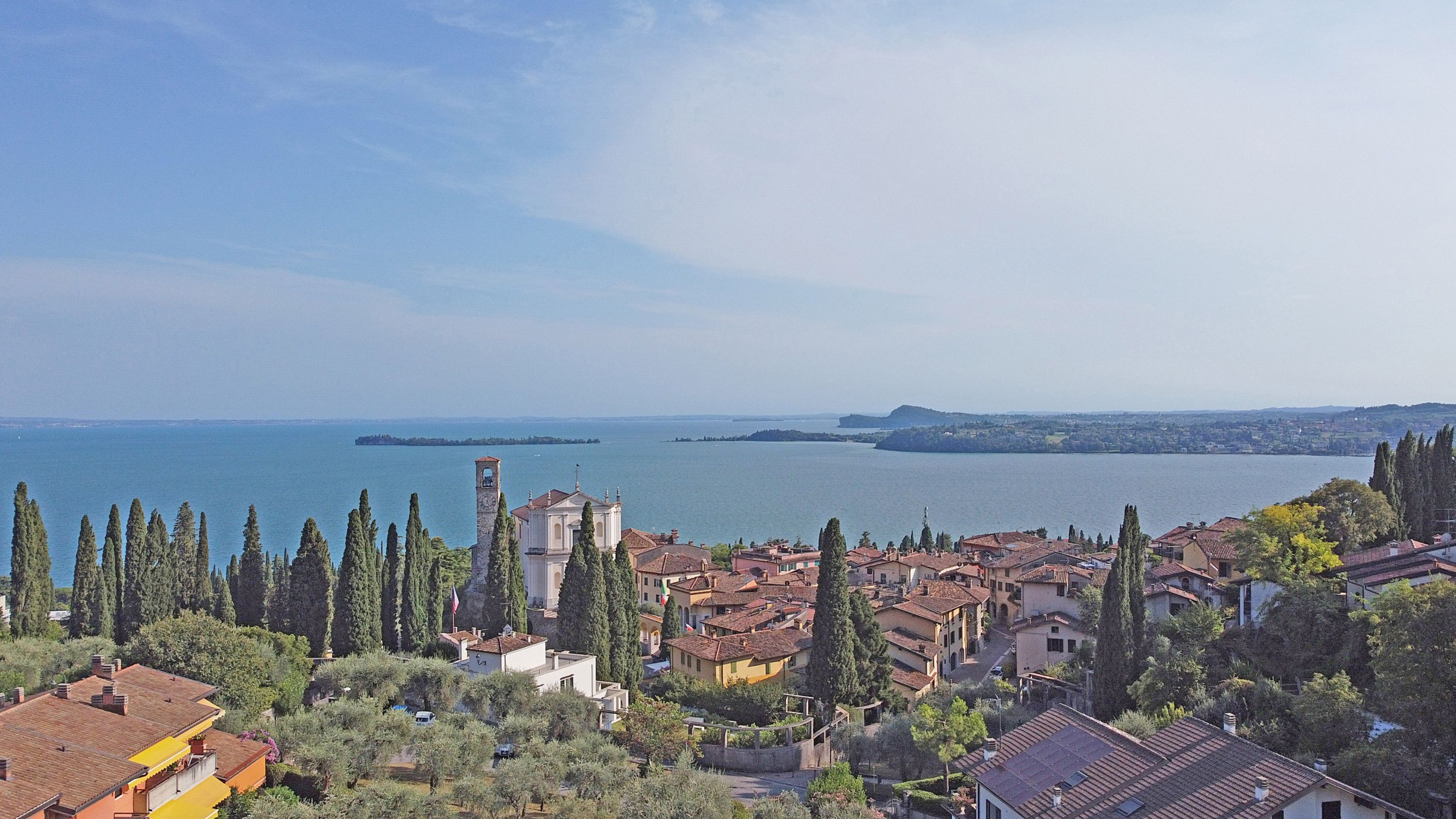 A coastal town with historic buildings, a prominent bell tower, and a view of the sea.
