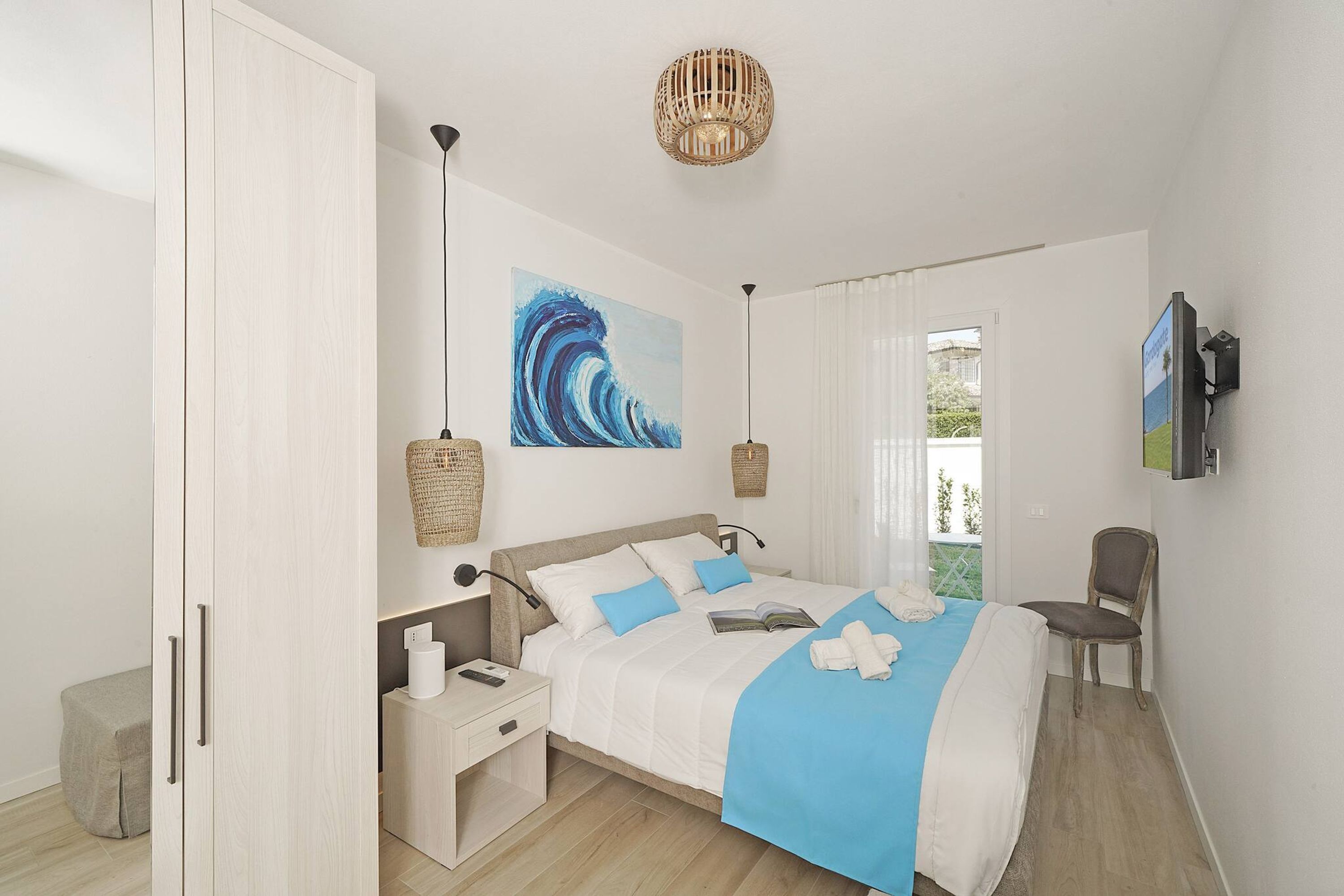 A modern bedroom with a bed, bedside tables, a chair, a painting, and a view of the outdoors.