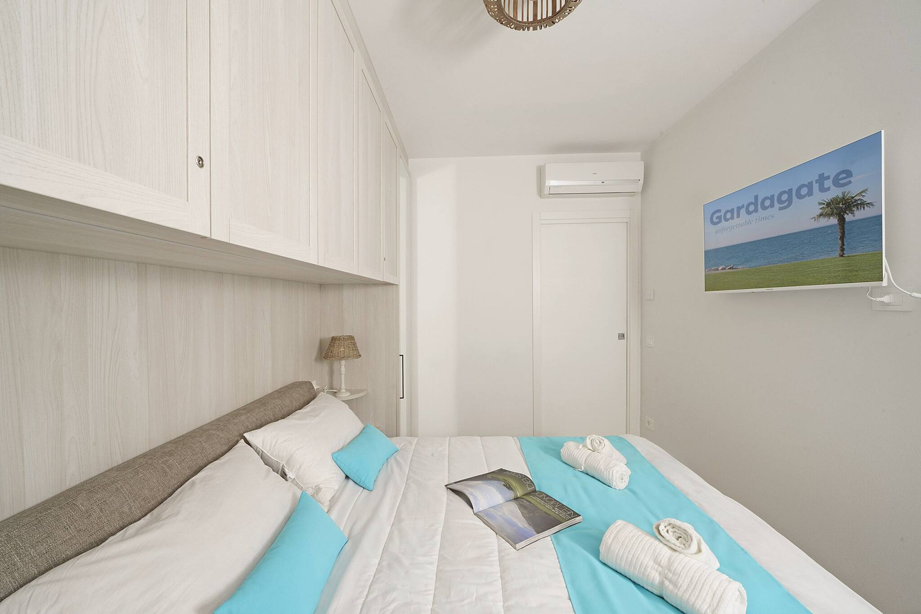 Un dormitorio ordenado con una cama, almohadas, un libro y toallas.