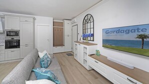 Una cocina moderna con armarios blancos, horno empotrado y comedor con mesa y sillas de madera.