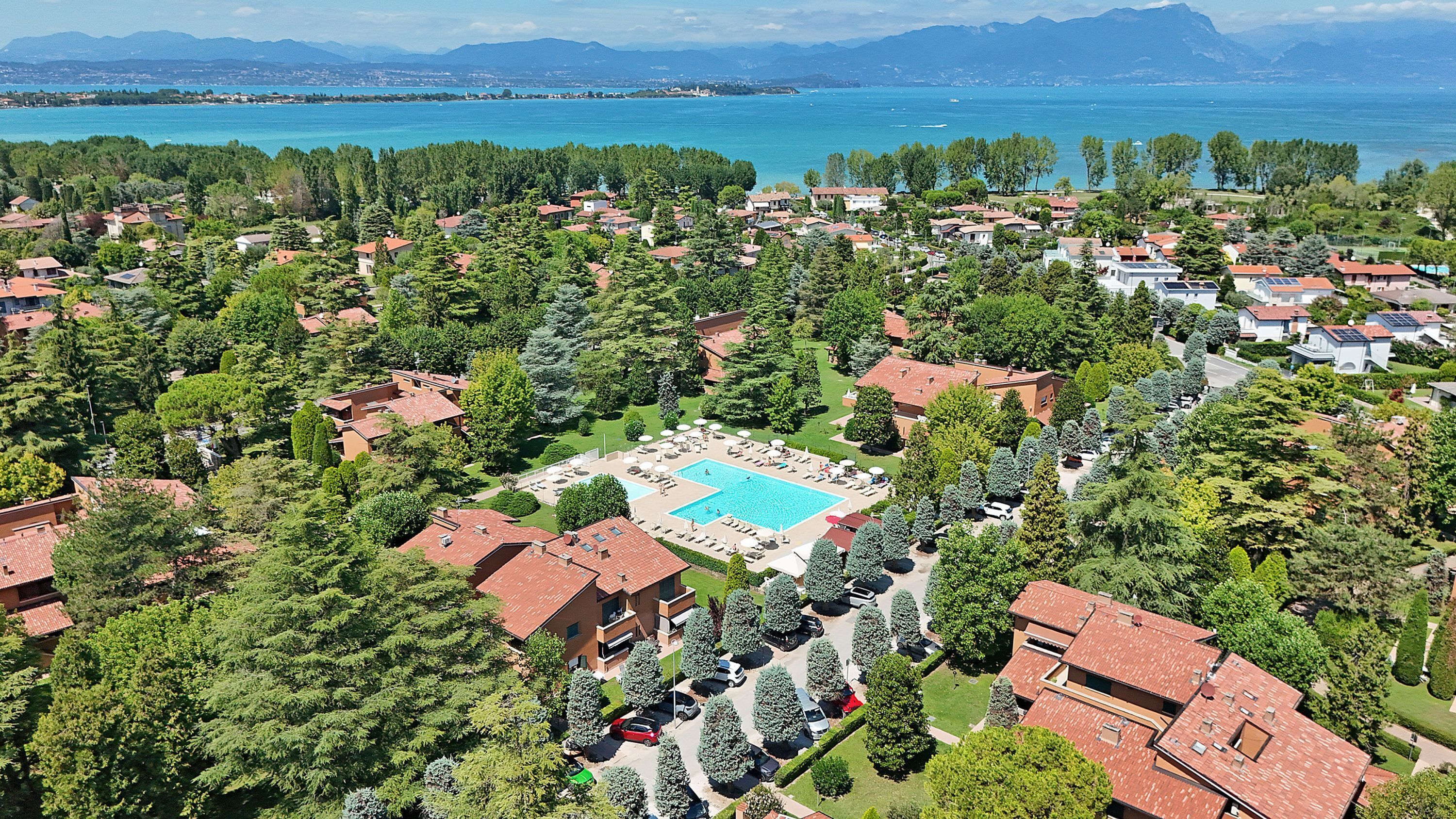 An aerial view of a residential area with a large swimming pool surrounded by houses and trees.