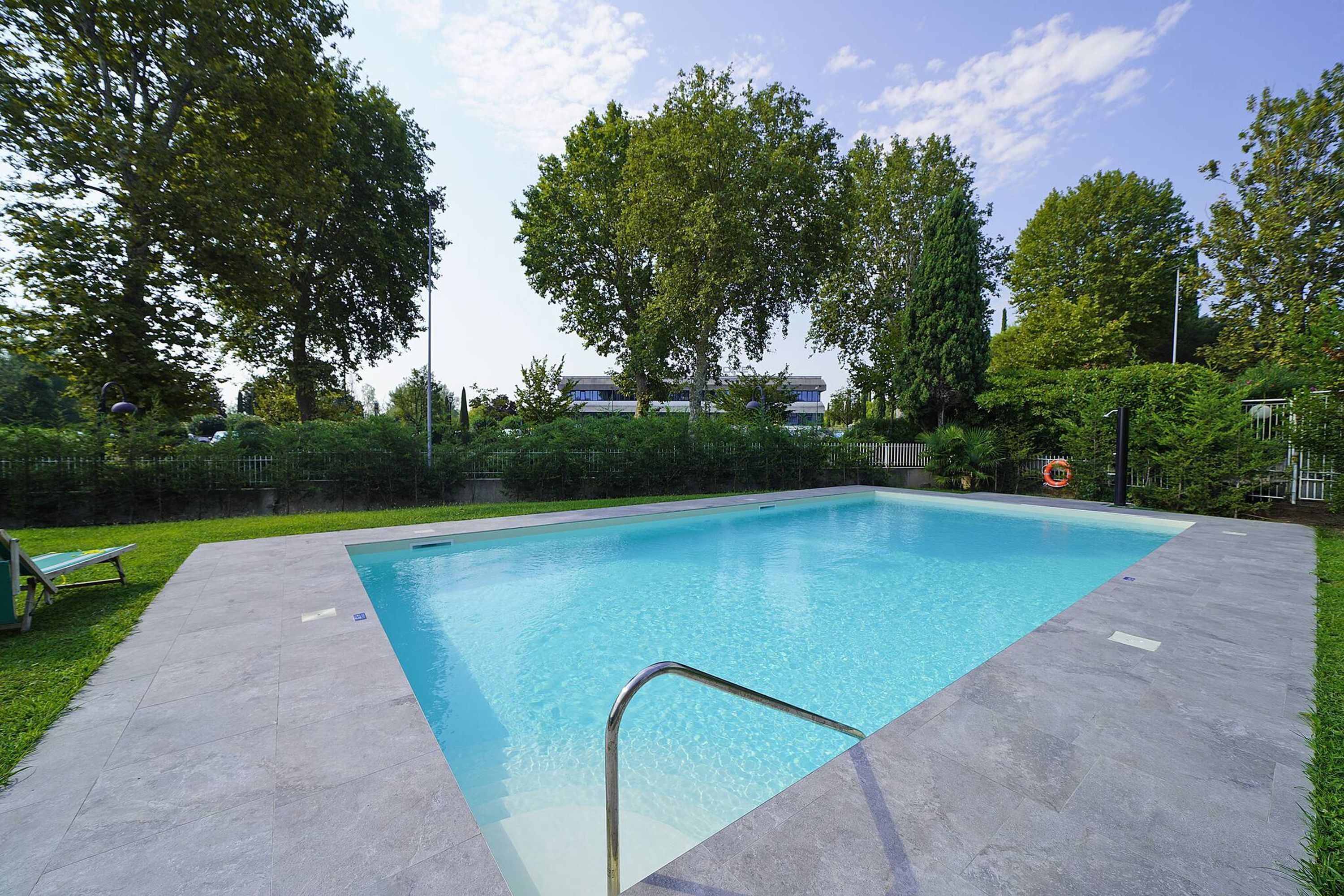 Una piscina rettangolare con una scaletta metallica in primo piano, circondata da un solarium lastricato.
