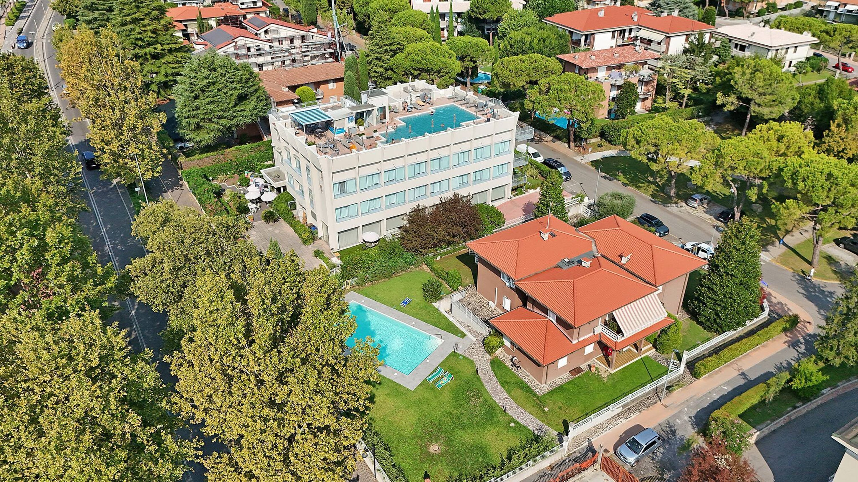 An aerial view of a residential area with a large building featuring a rooftop pool and a smaller adjacent building with a red roof.