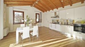 Une cuisine moderne avec des meubles blancs, un coin repas doté d’une table et de chaises blanches, et un plafond en bois.
