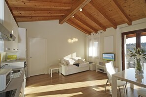 A modern living room with a white sofa, a dining table, and a kitchen area with a microwave. - Albatros B8 in Toscolano-maderno (Toscolano Maderno)