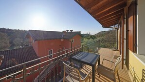 Un balcon avec une table et des chaises, donnant sur un bâtiment rouge et un paysage pittoresque.
