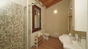 Une salle de bain avec une douche à parois de verre, des toilettes, un lavabo avec un miroir et une étagère en bois où sont posées des serviettes.