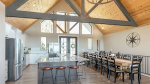Una cocina amplia con una isla grande, taburetes de bar y un comedor con una mesa de madera larga y sillas.