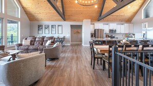 Un espacio habitable amplio con techo de madera, un comedor con una mesa grande y sillas, y una cocina con armarios blancos y electrodomésticos modernos.