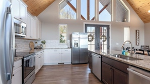 A modern kitchen with white cabinets, stainless steel appliances, a wooden ceiling, and large windows. - Amazing Table Rock Views - Sleeps 32 - indoor pool (Branson)