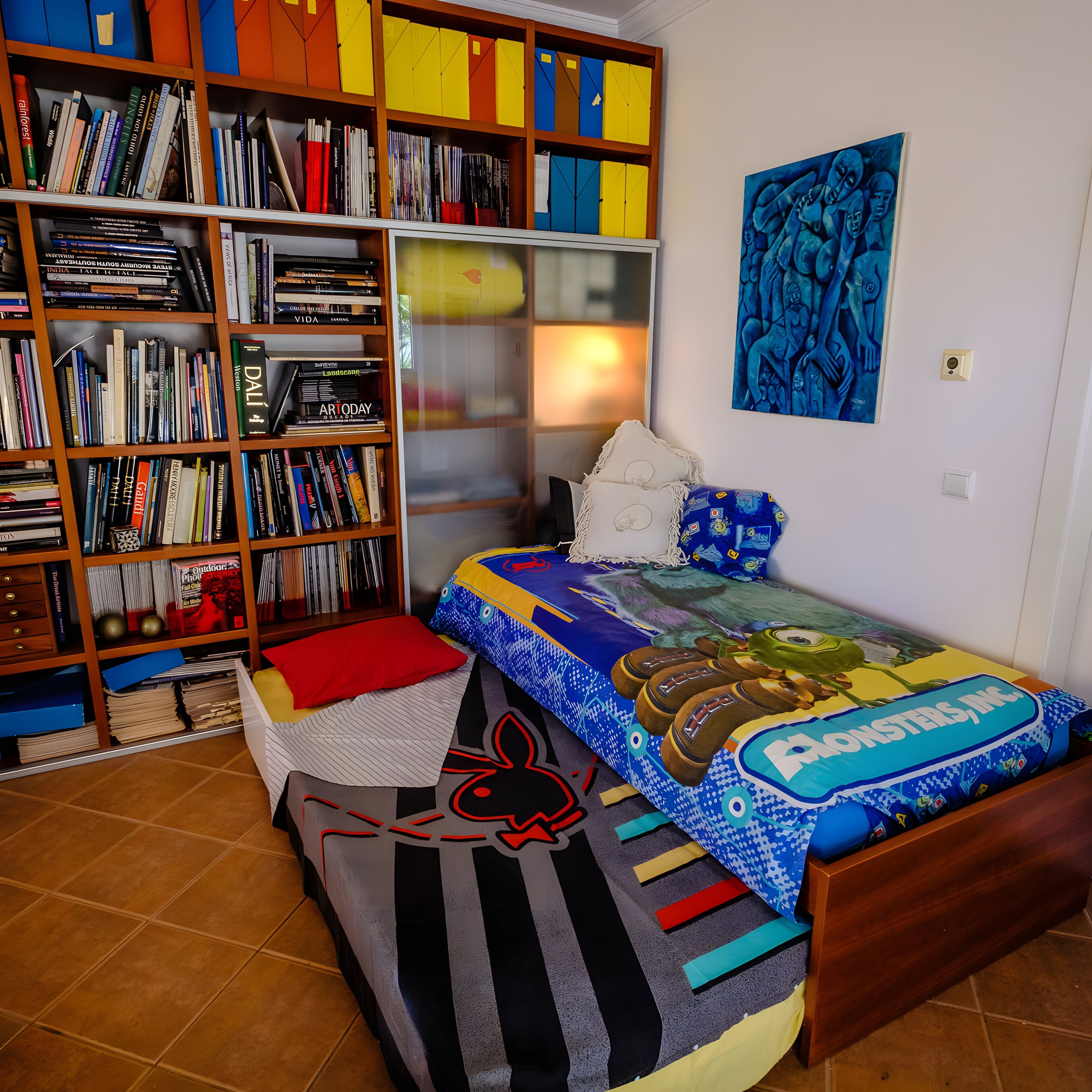 A bedroom with a bed, a bookshelf, a painting, and a window.
