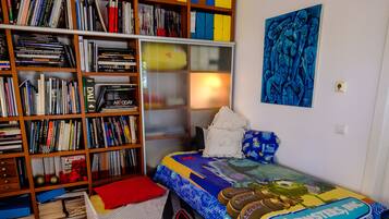 A bedroom with a bed, a bookshelf, a painting, and a window.