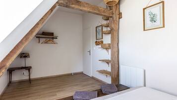 A room with a sloped ceiling, wooden beams, a bed with pillows, a hanging basket, and a framed plant on the wall.