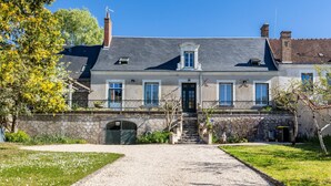 A two-story building with a stone facade, a gravel driveway, and a small bridge leading to the entrance. - Charming Cottage with Spa for 8–10 Guests, Near Loire Castles (Esvres)