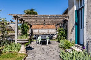 Un patio con pérgola, mobiliario exterior, una fuente de piedra y un edificio con ventana.