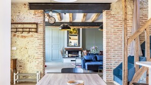 A rustic interior with exposed brick walls, a wooden dining table, and a blue sofa. - Charming Cottage with Spa for 8–10 Guests, Near Loire Castles (Esvres)