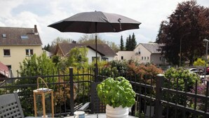 Un balcon avec une plante en pot, une table avec une tasse et un parapluie noir.